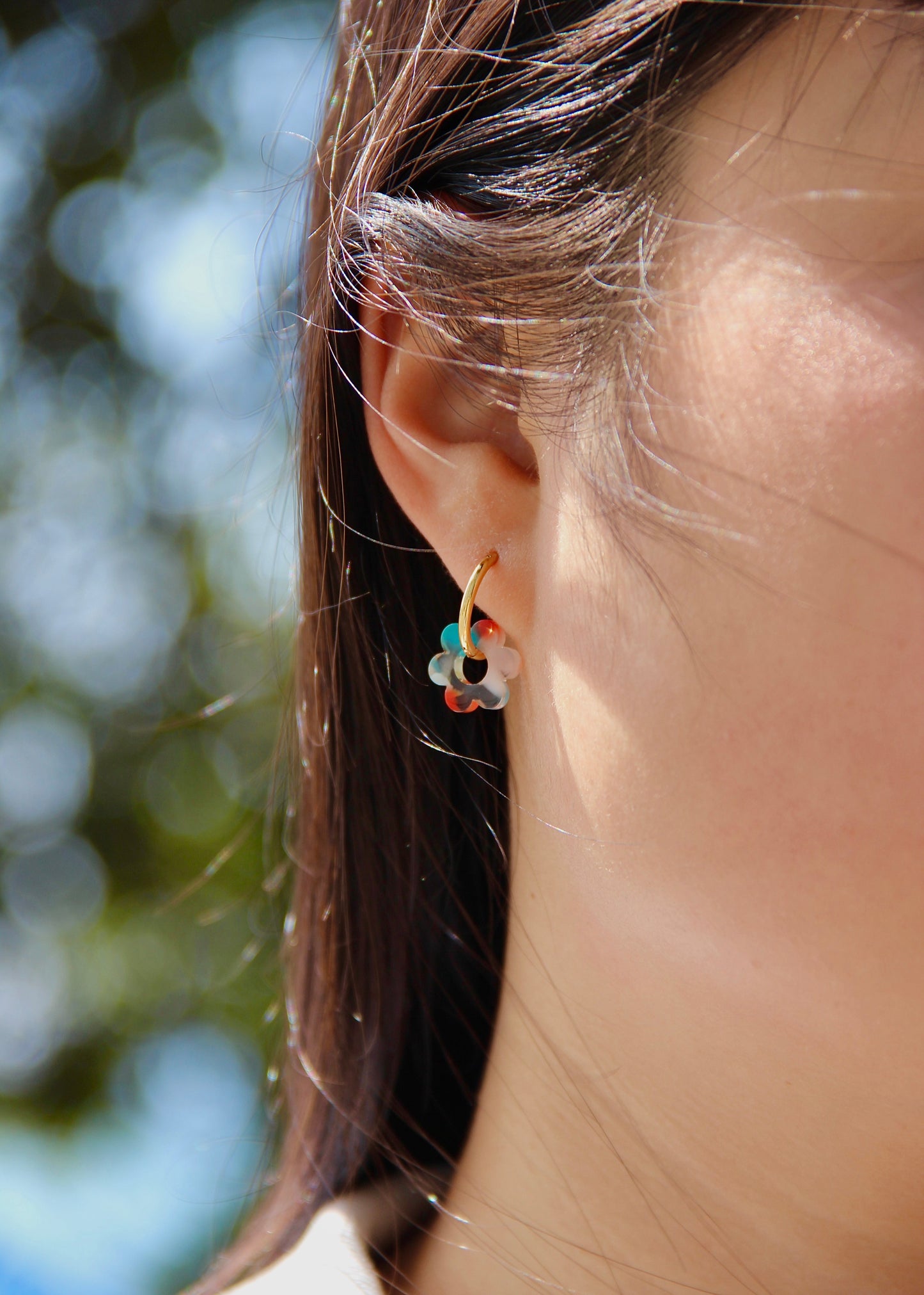 Orecchini ad anello in acciaio dorato con chiusura a scattino e ciondolo a forma di fiore in resina – colori rosa, azzurro, crema, arancione, fantasia blu-arancione e fantasia blu-verde – stile giocoso, primaverile ed estivo – bijoux leggeri e colorati.