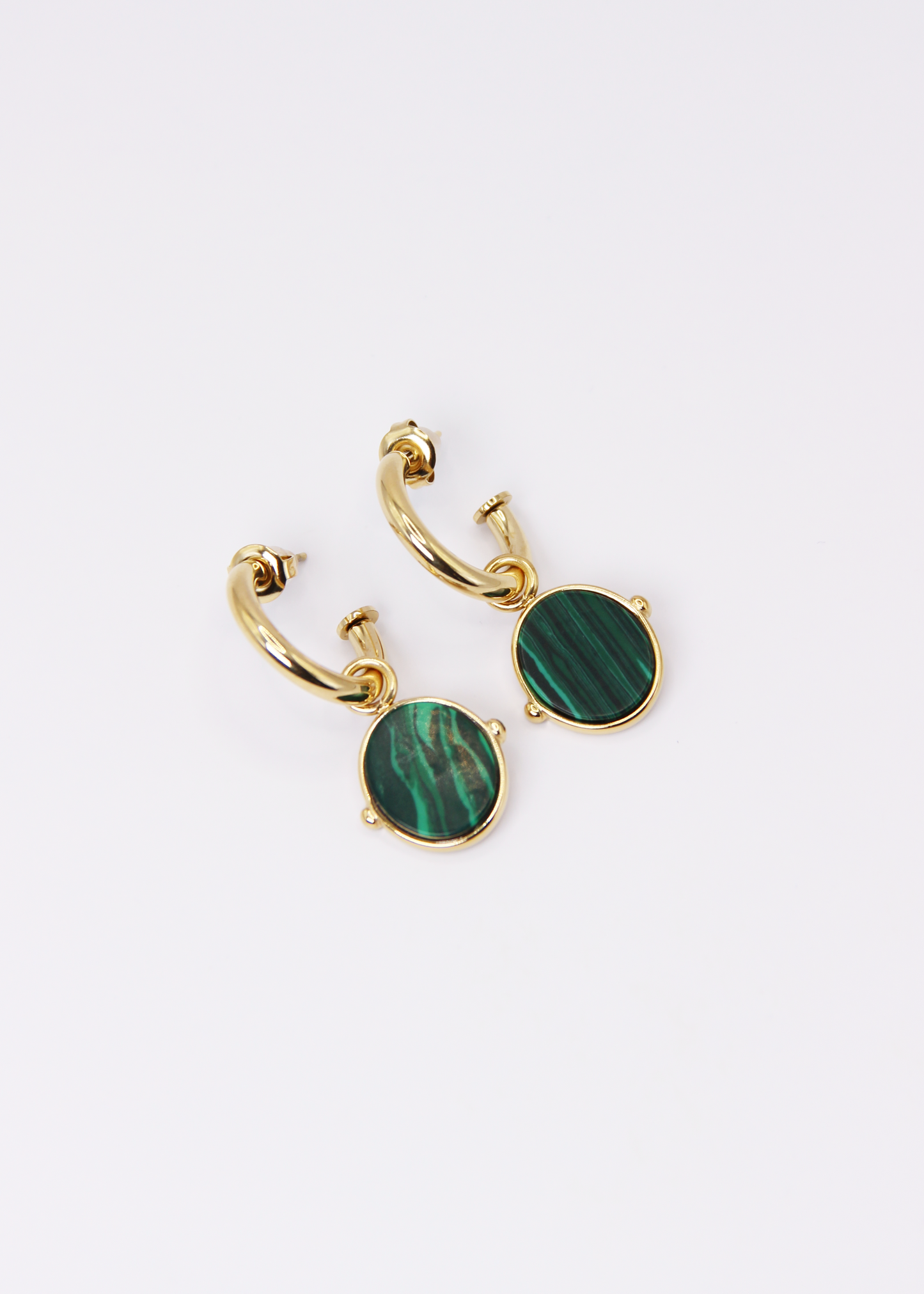 Orecchini a cerchio in acciaio placcato oro con pendente ovale in pietra dura naturale. Modello elegante con chiusura a perno, disponibile in vari colori tra cui occhio di tigre, malachite e opalite. Ogni pietra presenta leggere variazioni naturali di colore e venature.