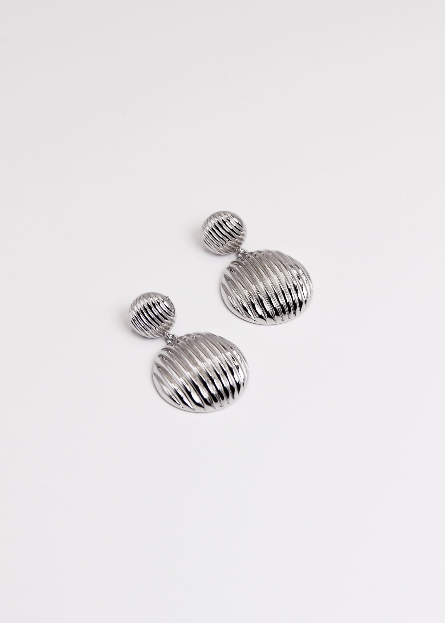 Orecchino pendente chunky con chiusura a perno, composto da due bottoni con texture rigata. Realizzato in argento 925, disponibile anche placcato oro per un tocco di eleganza in più. La lunghezza totale dell'orecchino è di 3,8 cm, con un diametro del bottone inferiore di 2,3 cm, ideale per un look sofisticato e moderno.