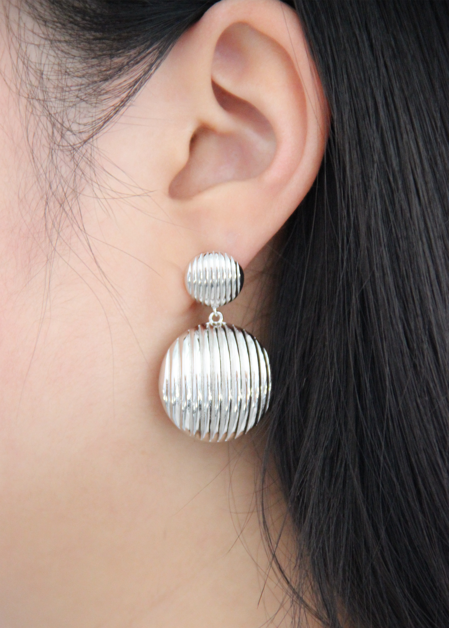 Orecchino pendente chunky con chiusura a perno, composto da due bottoni con texture rigata. Realizzato in argento 925, disponibile anche placcato oro per un tocco di eleganza in più. La lunghezza totale dell'orecchino è di 3,8 cm, con un diametro del bottone inferiore di 2,3 cm, ideale per un look sofisticato e moderno.