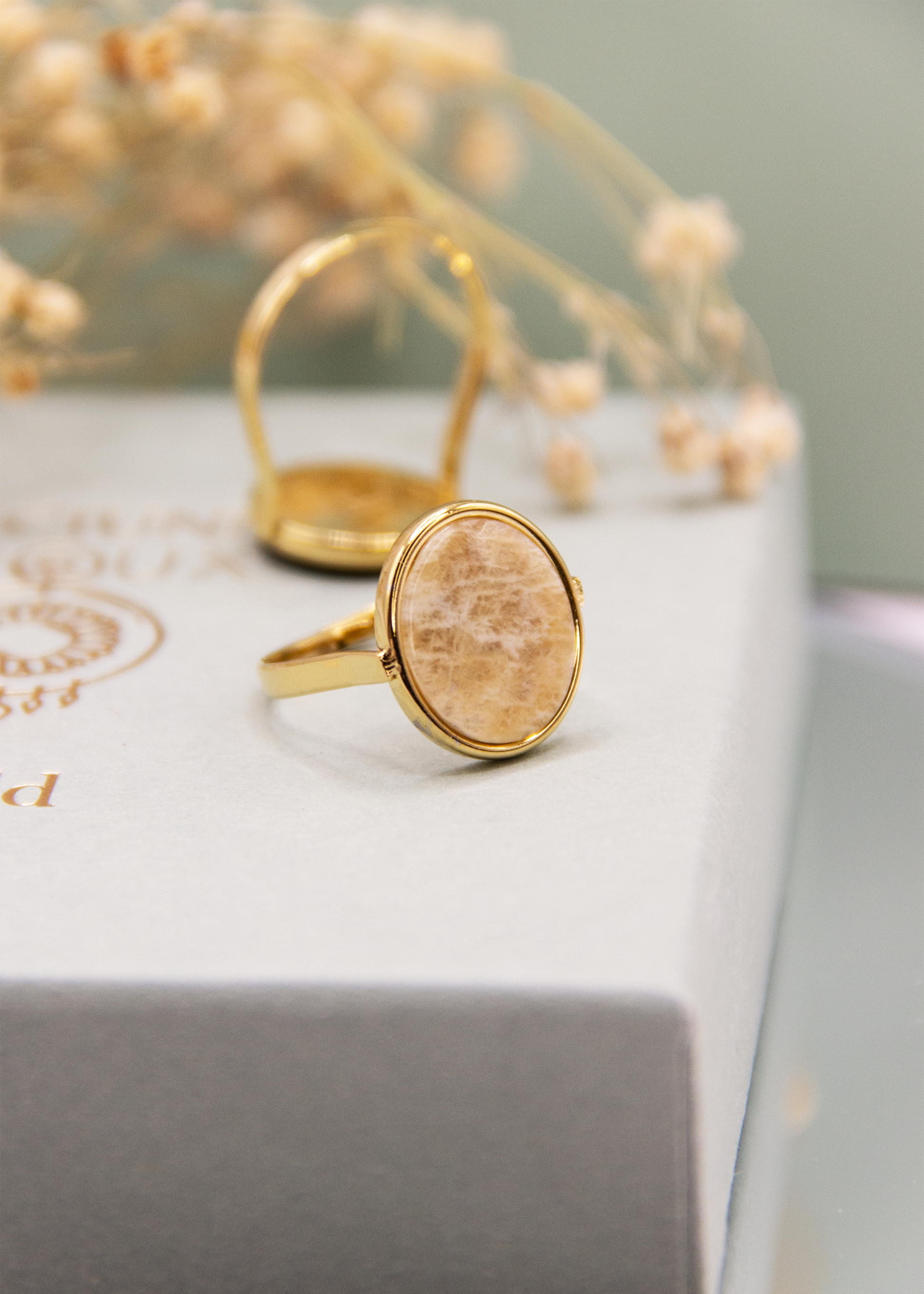 Anello ovale in acciaio placcato oro con pietra dura naturale. Fascia sottile e regolabile, montatura liscia che avvolge la pietra. Disponibile in diversi colori, dal design elegante e raffinato