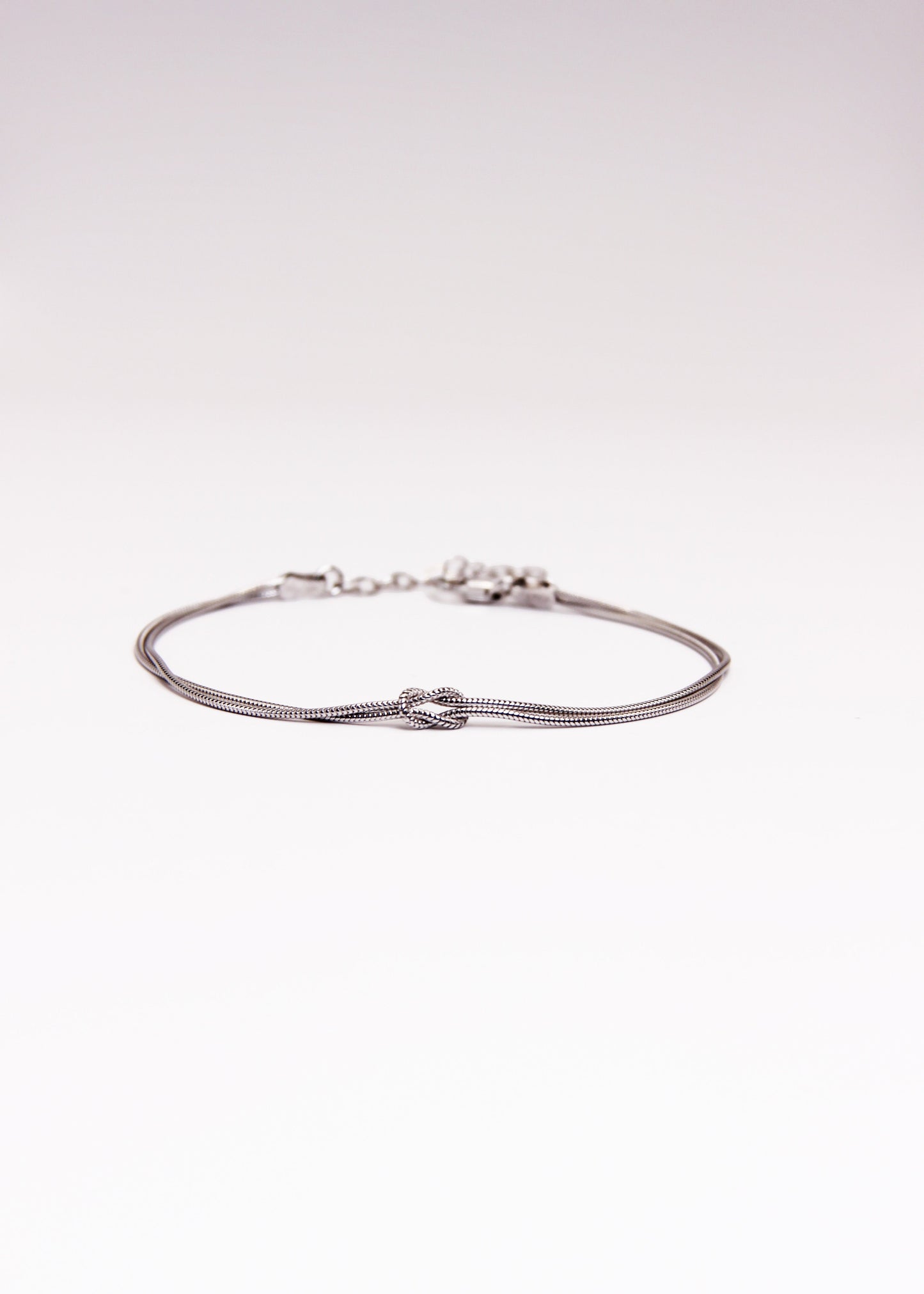 Bracciale in argento 925 con nodo, composto da due fili intrecciati. Disponibile anche in versione placcato oro. La lunghezza del bracciale è regolabile, per una vestibilità personalizzata.