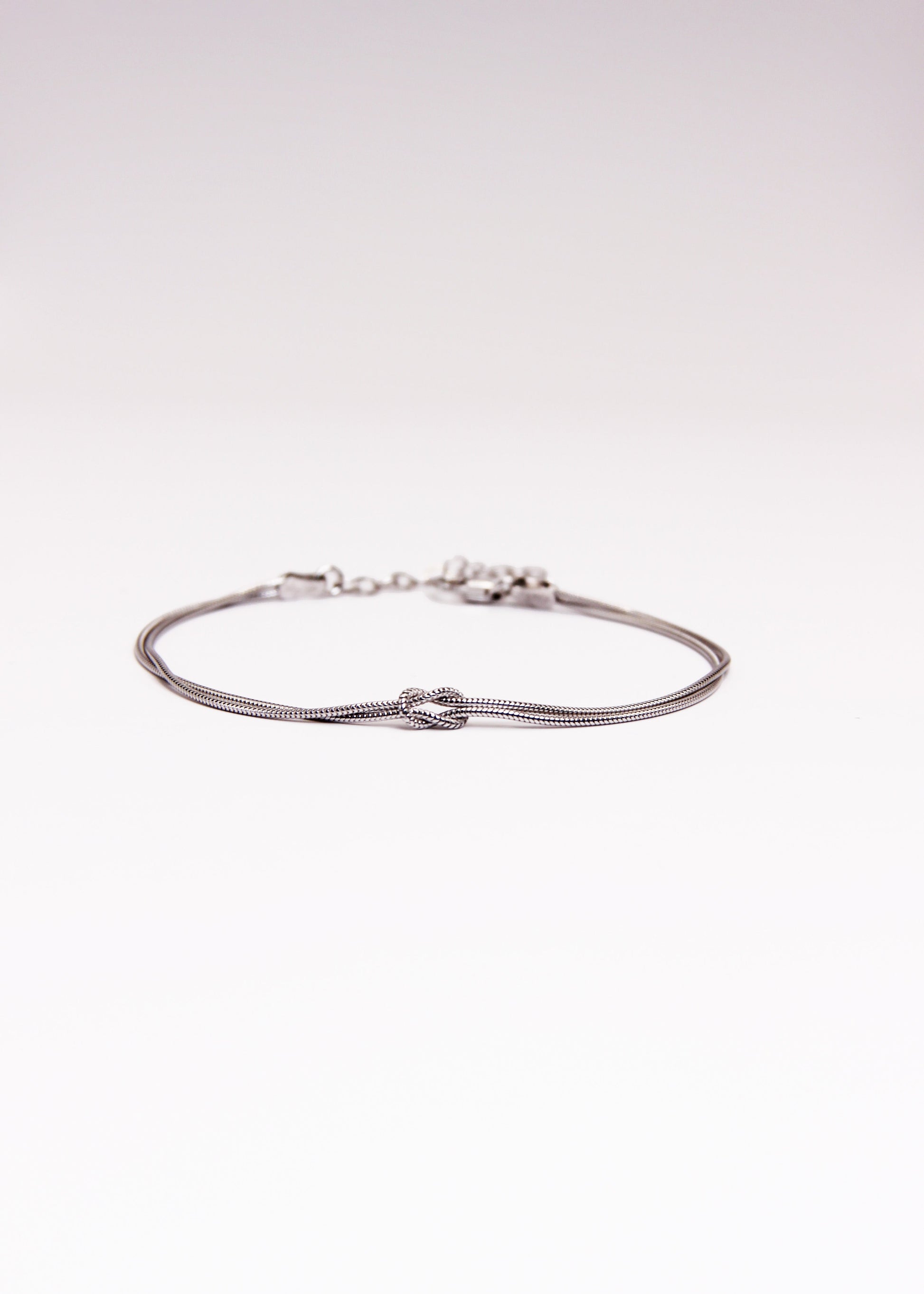 Bracciale in argento 925 con nodo, composto da due fili intrecciati. Disponibile anche in versione placcato oro. La lunghezza del bracciale è regolabile, per una vestibilità personalizzata.