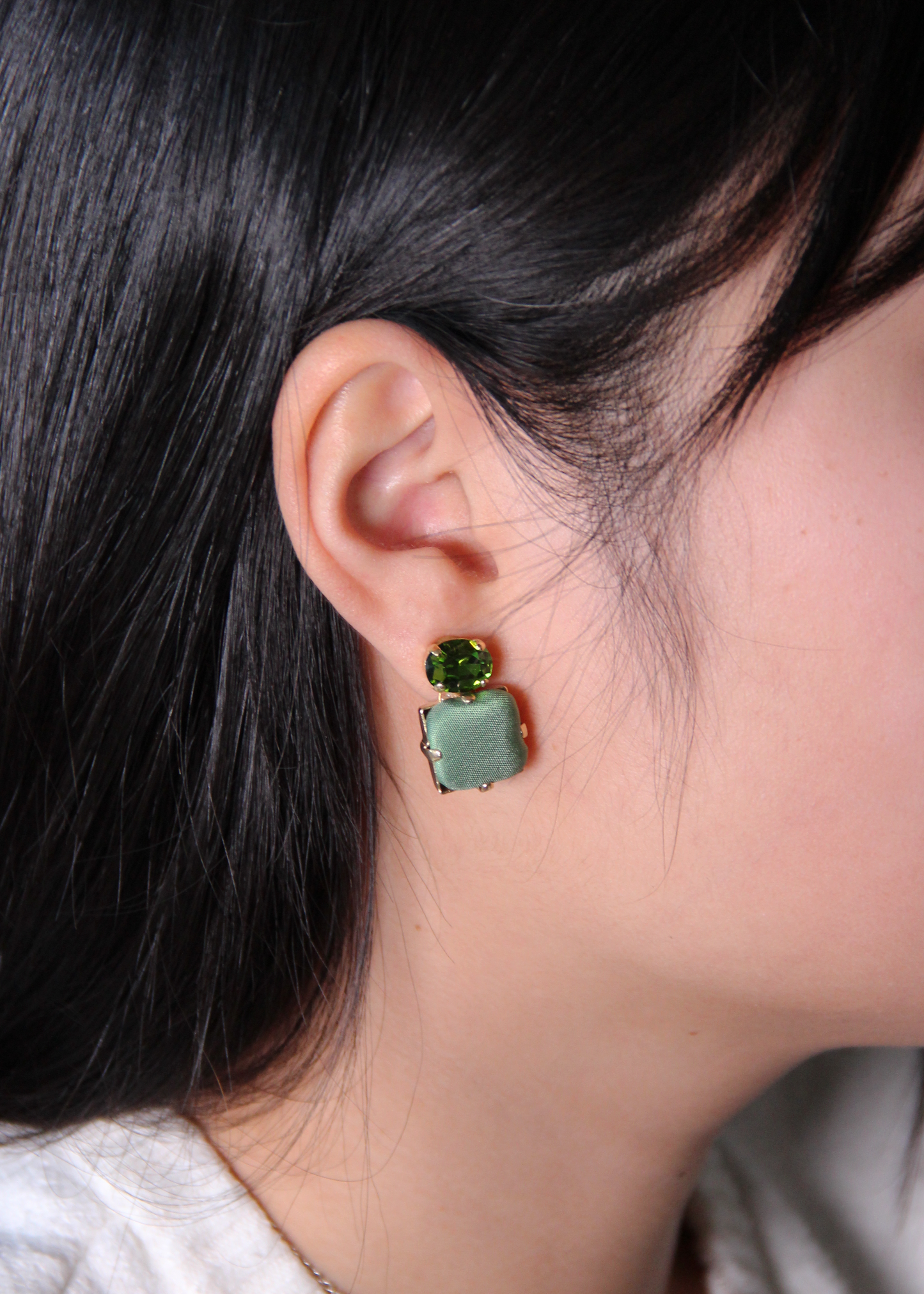 Orecchini verde salvia eleganti fatti a mano da Laura Sciunnach Bijoux, modello Metropolitan Siviglia con bottone quadrato in stoffa verde salvia e cristallo ovale verde tono su tono, design geometrico leggero e raffinato.