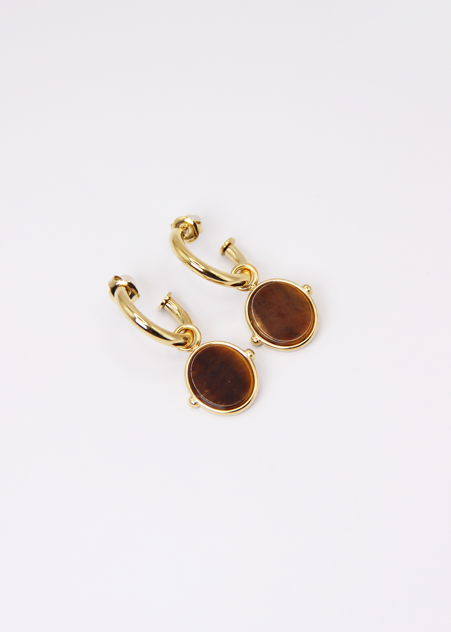 Orecchini a cerchio in acciaio placcato oro con pendente ovale in pietra dura naturale. Modello elegante con chiusura a perno, disponibile in vari colori tra cui occhio di tigre, malachite e opalite. Ogni pietra presenta leggere variazioni naturali di colore e venature.