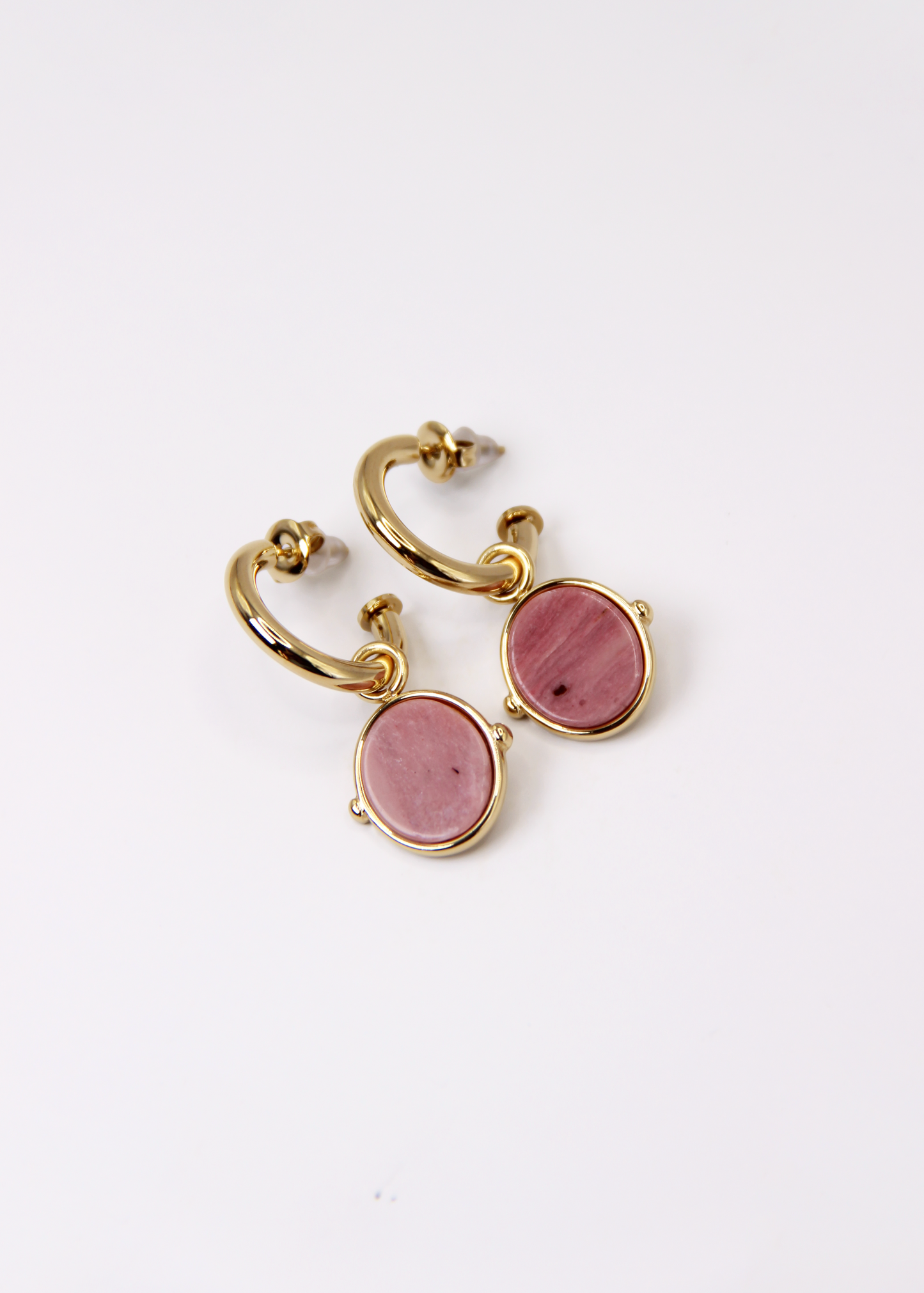 Orecchini a cerchio in acciaio placcato oro con pendente ovale in pietra dura naturale. Modello elegante con chiusura a perno, disponibile in vari colori tra cui occhio di tigre, malachite e opalite. Ogni pietra presenta leggere variazioni naturali di colore e venature.