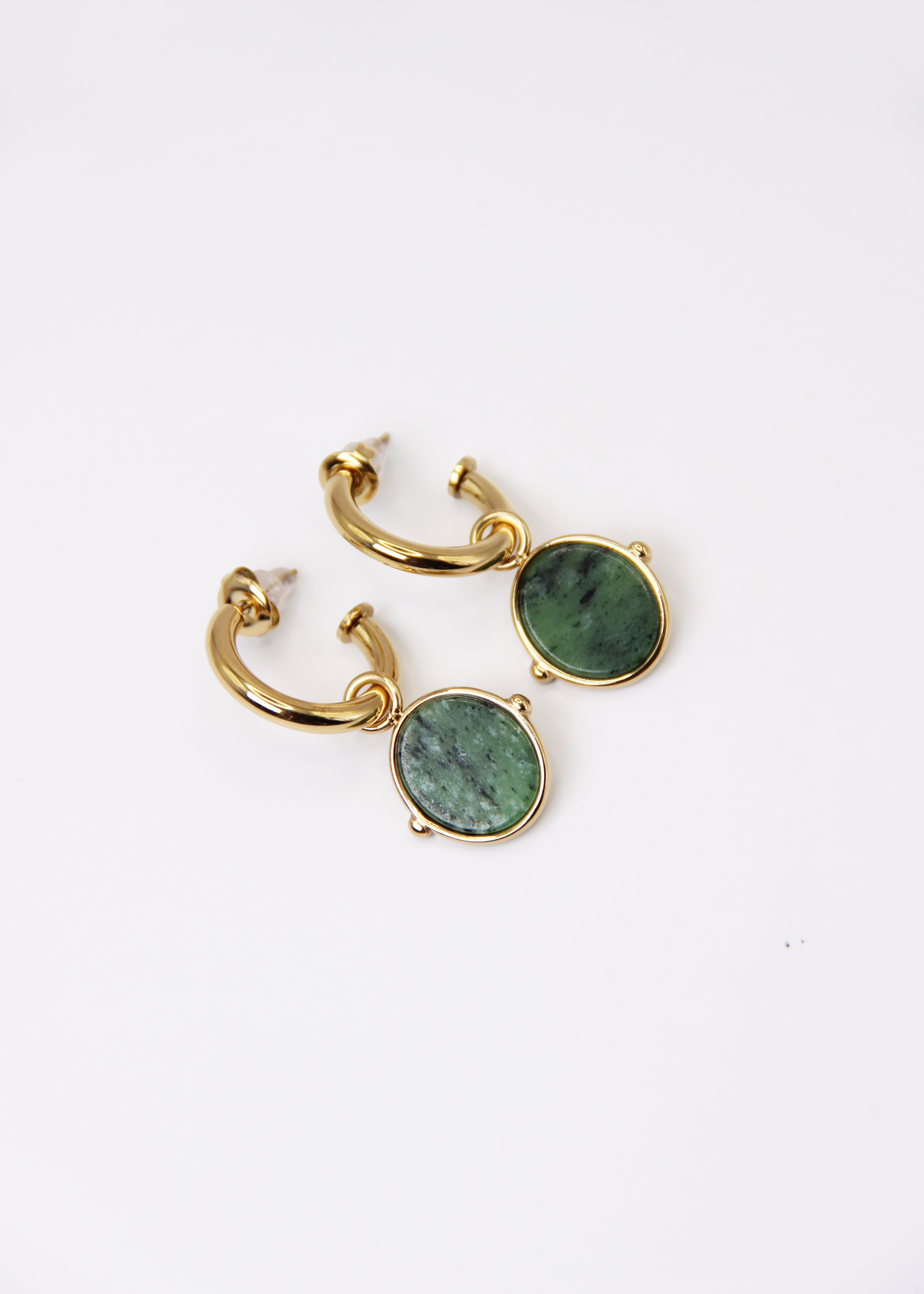 Orecchini a cerchio in acciaio placcato oro con pendente ovale in pietra dura naturale. Modello elegante con chiusura a perno, disponibile in vari colori tra cui occhio di tigre, malachite e opalite. Ogni pietra presenta leggere variazioni naturali di colore e venature.