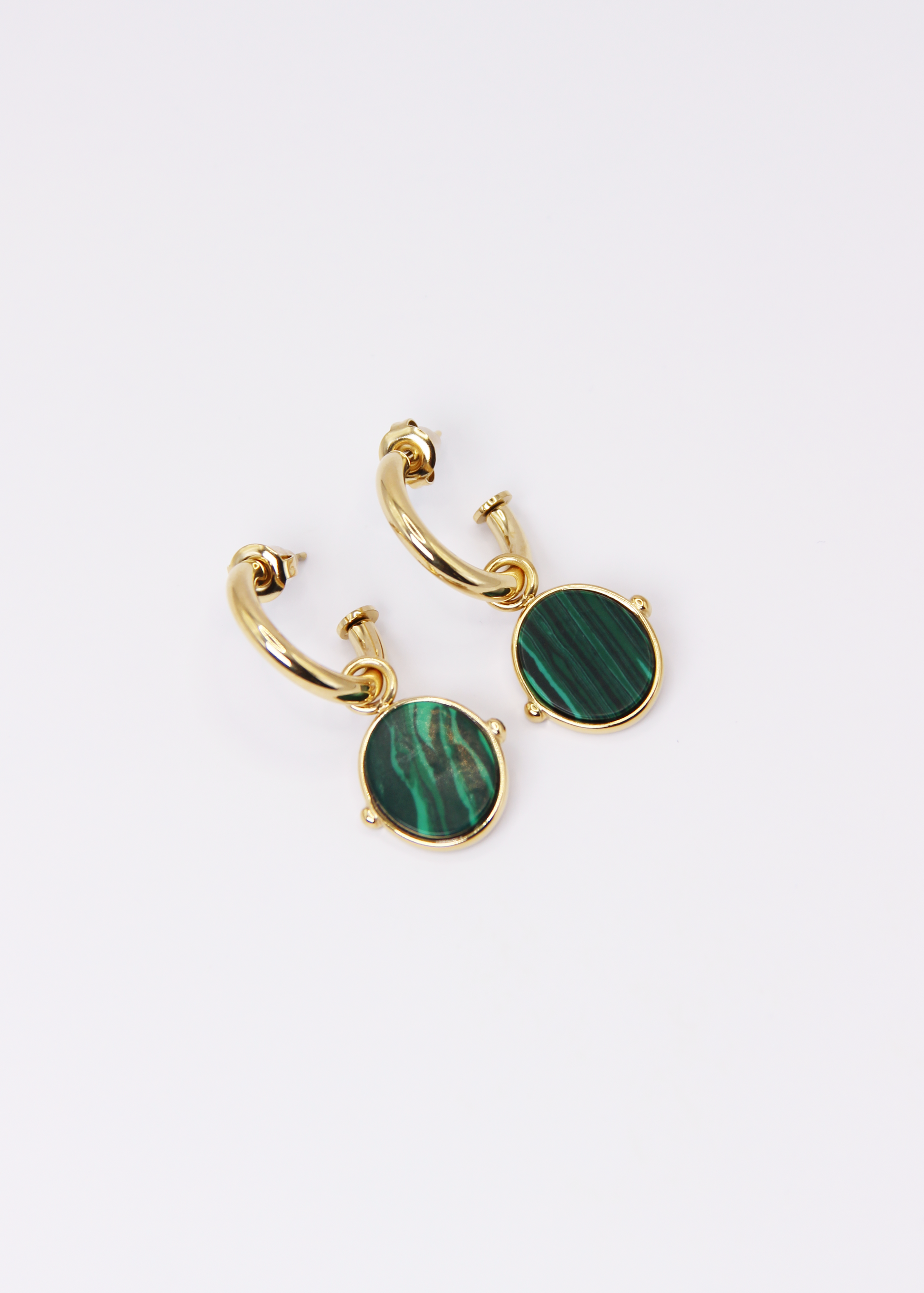 Orecchini a cerchio in acciaio placcato oro con pendente ovale in pietra dura naturale. Modello elegante con chiusura a perno, disponibile in vari colori tra cui occhio di tigre, malachite e opalite. Ogni pietra presenta leggere variazioni naturali di colore e venature.